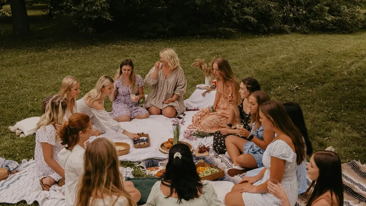 Un grupo de mujeres sentadas en círculo sobre mantas, compartiendo un picnic en un parque